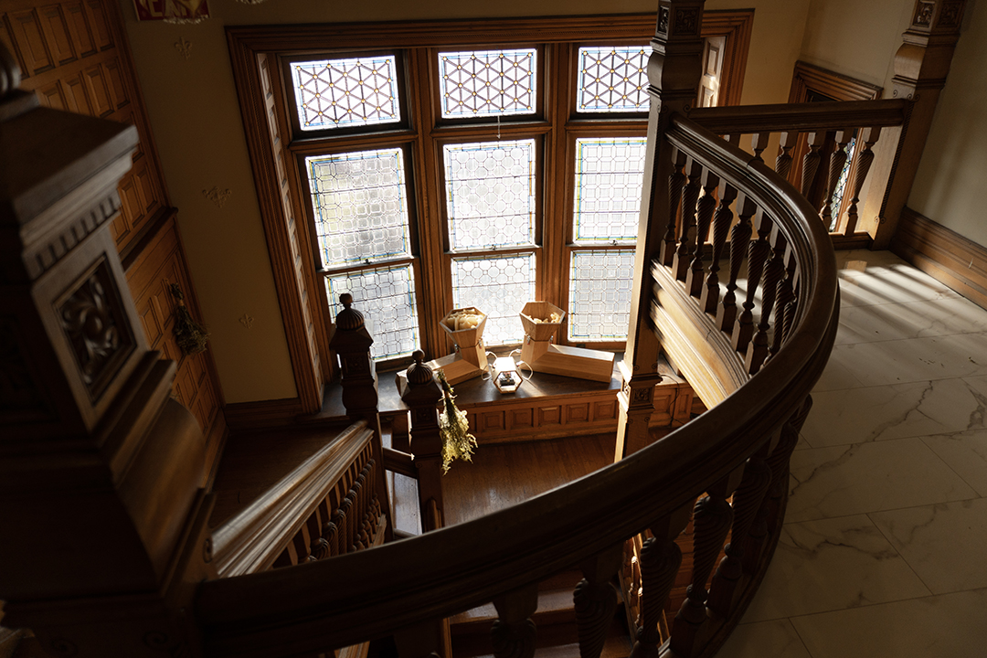 Looking over a curved wooden banister in a mansion, at "The Translation Machine", an interactive sound sculpture by artist Daric Gill.