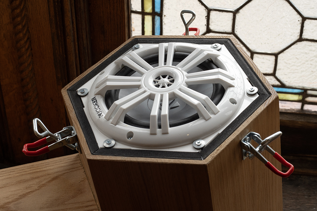 A white speaker mounted to the end of a hexagonal wooden tube used as speaker boxes.