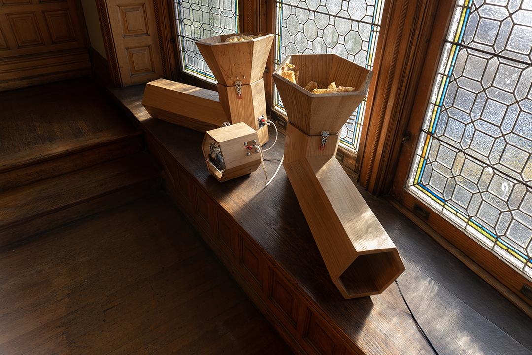 Two stylized acoustic speaker boxes create a 'V' shape on a window bench in a mansion.